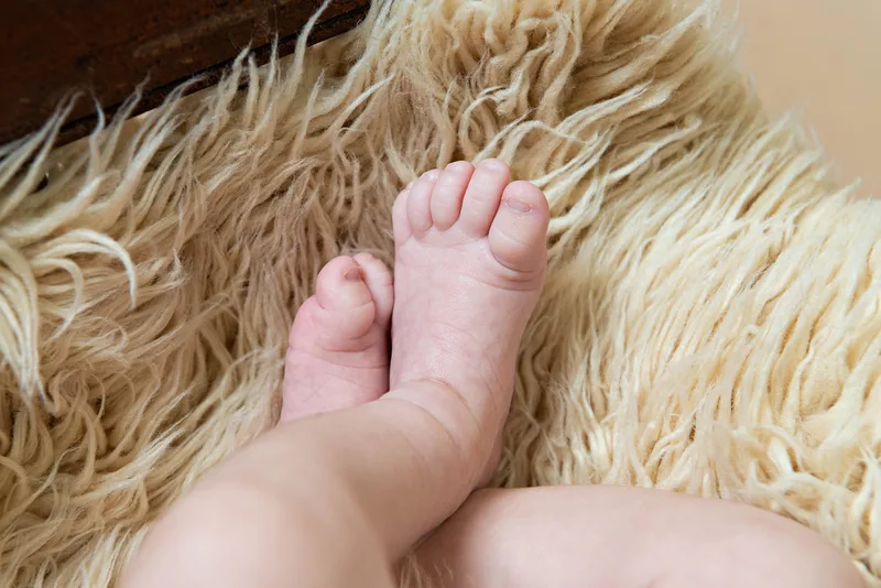 Color photo of a newborn baby photographed in a studio. The photo is a detail of his feet. The photo was taken by Laura Pea Photography, a Long Island based newborn photographer.