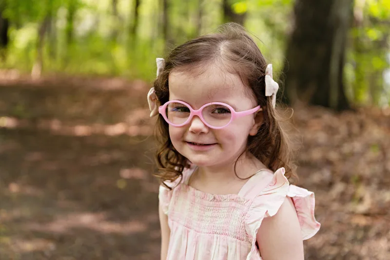 photo of a four year old girl smiling standing in a wooded park