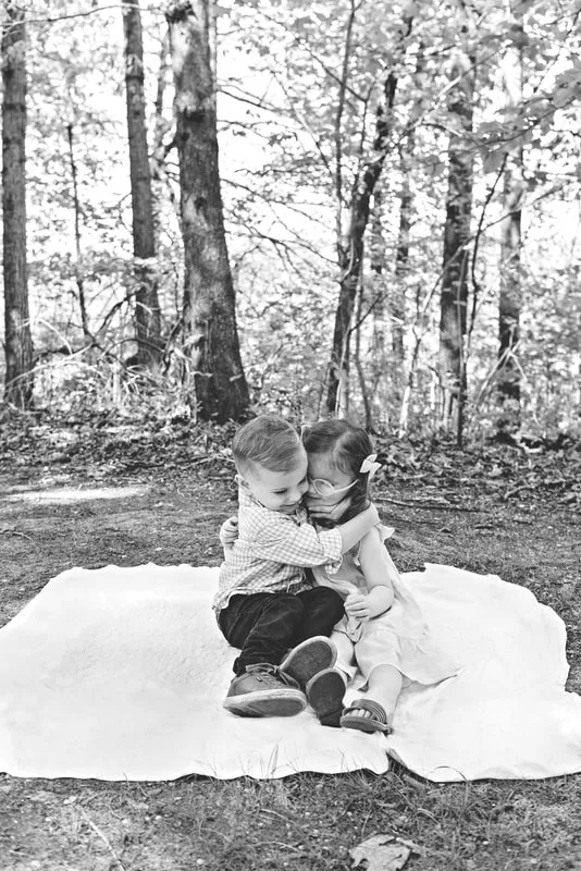 black and white photo of two four year old twin brother and sister  hugging on a blanket in a wooded park