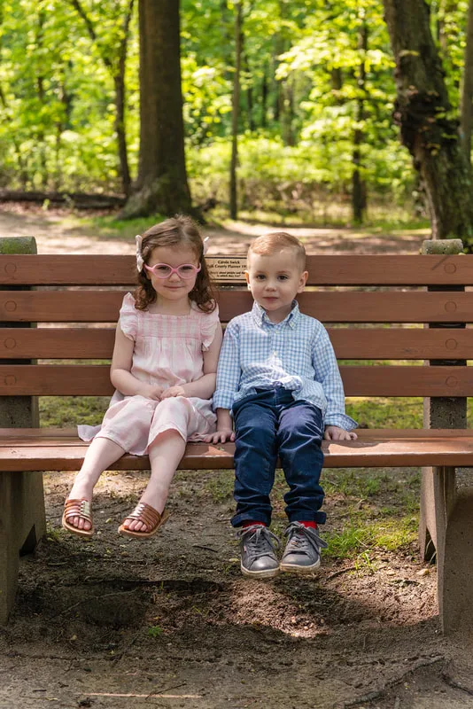 photo of two four year old twin brother and sister sitting on a bench in a wooded park