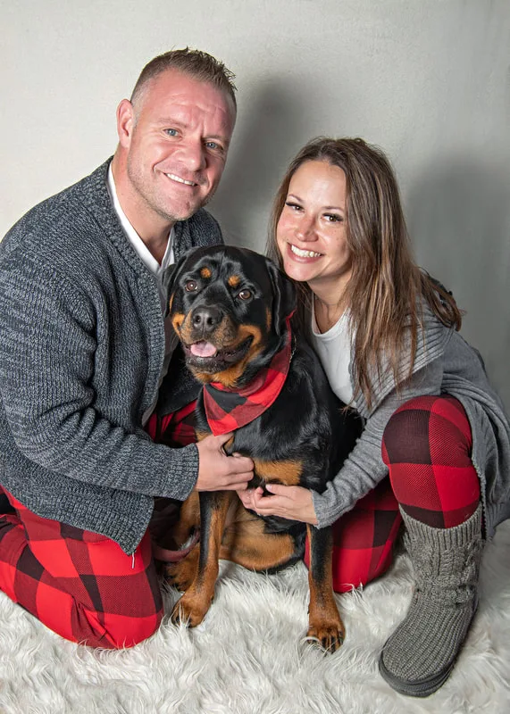 Color photo of a Rottweiler dog and his family against a white background. The photo was taken by Laura Pea Photography, a pet photographer on Long Island.