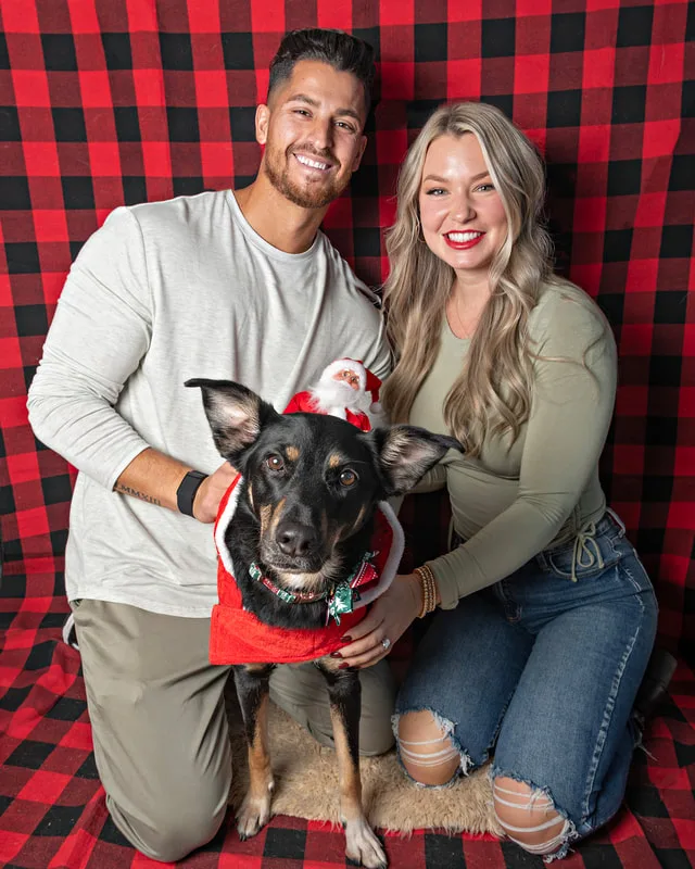 Color photo of a hound mix mutt dog with its family against a buffalo plaid background. The photo was taken by Laura Pea Photography, a pet photographer on Long Island.