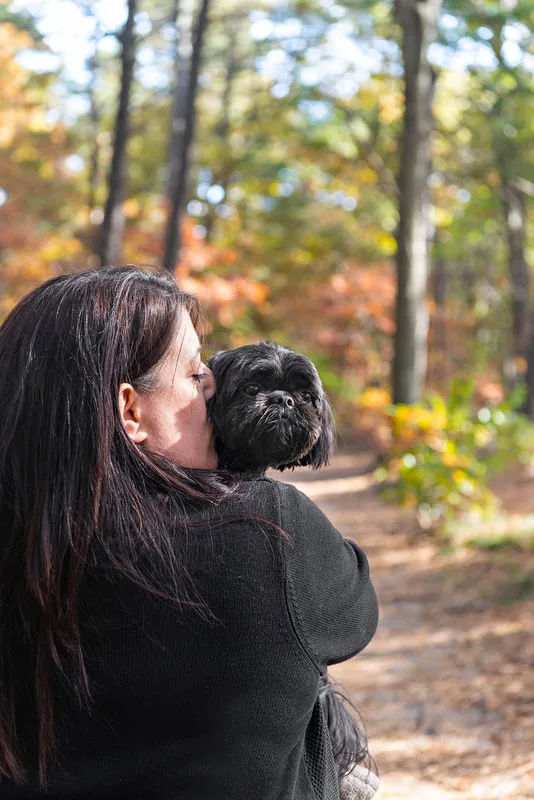 photo of a black shih tzu dog in the woods with his mom from behind