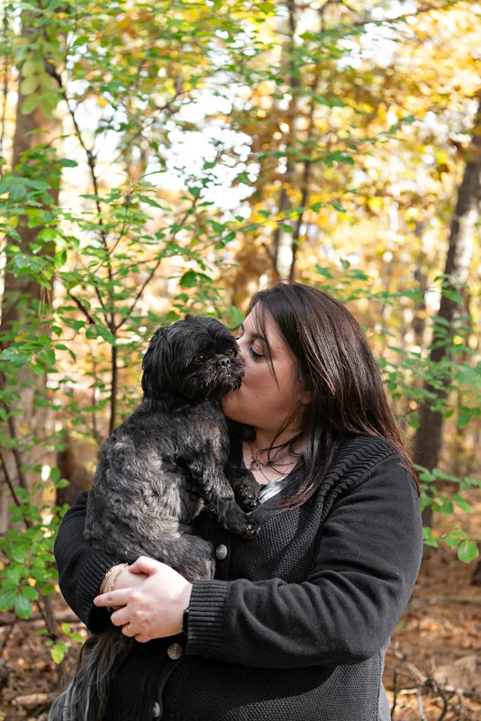 photo of a black shih tzu dog in the woods in his mom's arms 
