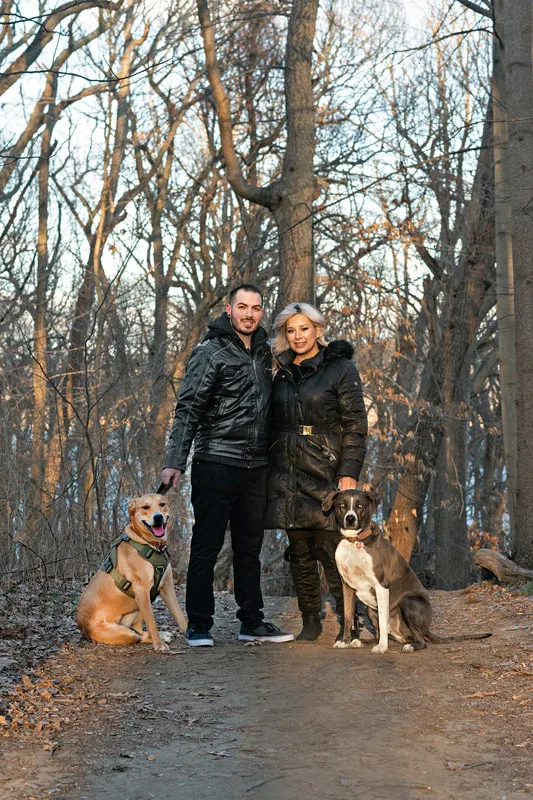 photo of a man, a woman, a grey and white labrador pit bull mix dog and a yellow labrador pit bull mix dog standing on a path in the woods