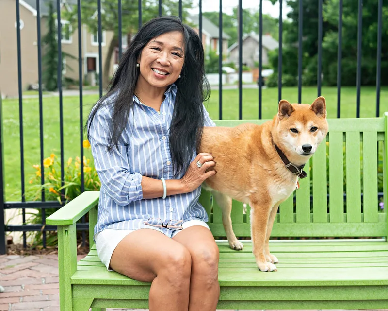 photo of an Asian woman with a Shiba Inu dog sitting on a green bench