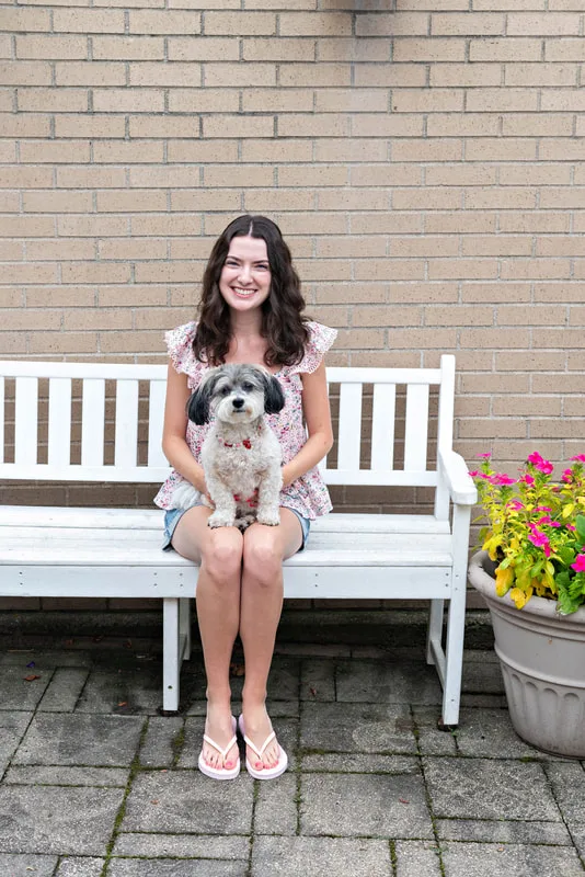 color photo of a girl and a dog on a white bench next to flowers. The photo was taken at West Islip Public Library by Long Island Pet Photographer Laura Pea Photography. 