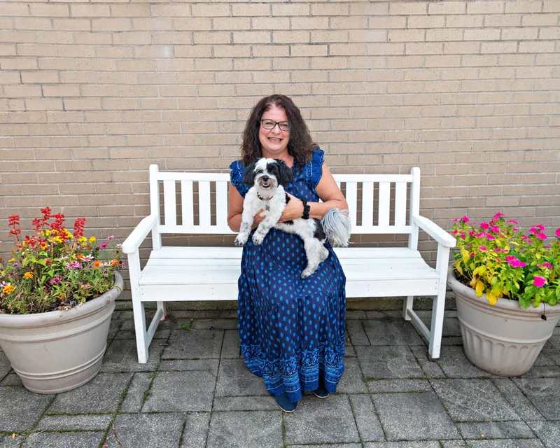 color photo of a mixed breed dog and owner on a white bench next to flowers. The photo was taken at West Islip Public Library by Long Island Pet Photographer Laura Pea Photography. 