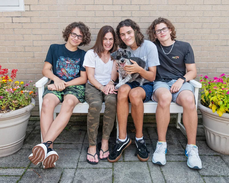  color photo of a terrier dog and family on a white bench next to flowers. The photo was taken at West Islip Public Library by Long Island Pet Photographer Laura Pea Photography. 