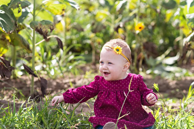 one year old baby girl sitting in a sunflower field on long island. Photo taken by Laura Pea Photography