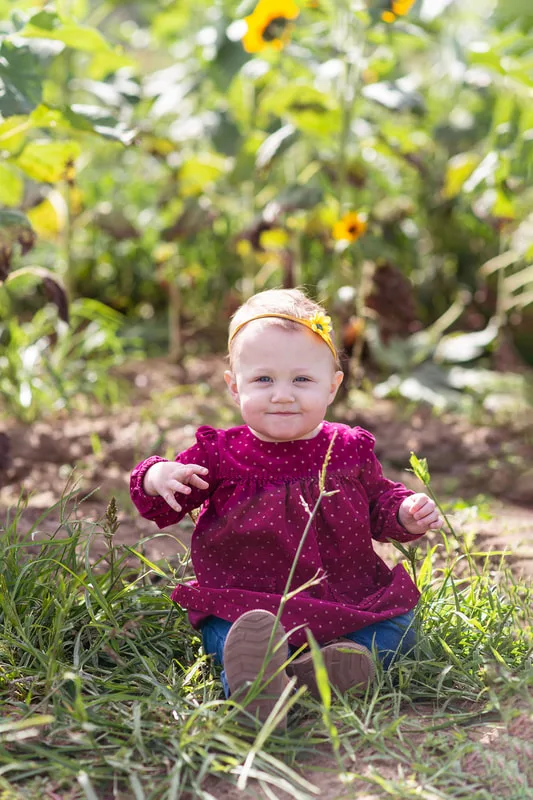 one year old baby girl sitting in a sunflower field on long island. Photo taken by Laura Pea Photography