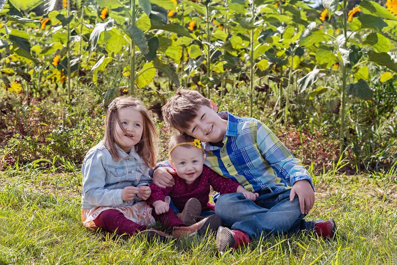 3 siblings posing in a sunflower field on long island. Photo by Laura Pea Photography