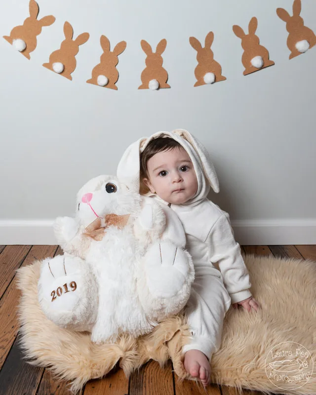picture of baby boy's first easter photo session in an easter bunny costume posing with rabbit stuffed animal