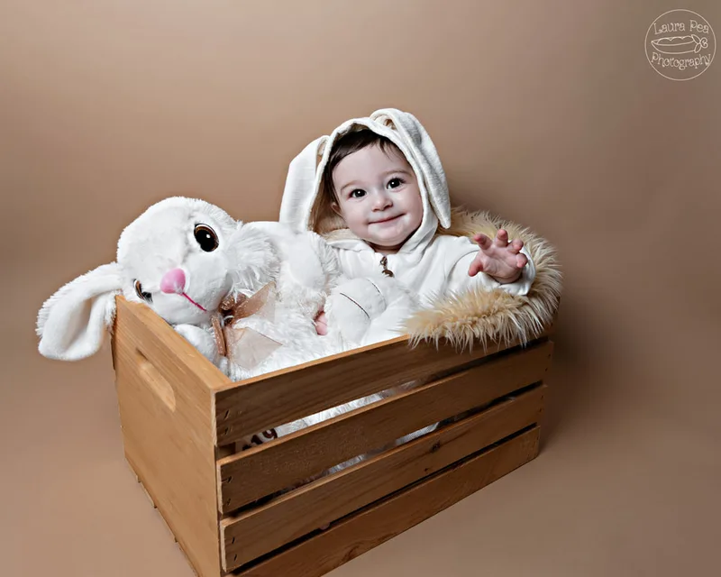 picture of baby boy's first easter photo session in an easter bunny costume smiling at the camera sitting in a wooden crate with a rabbit stuffed animal