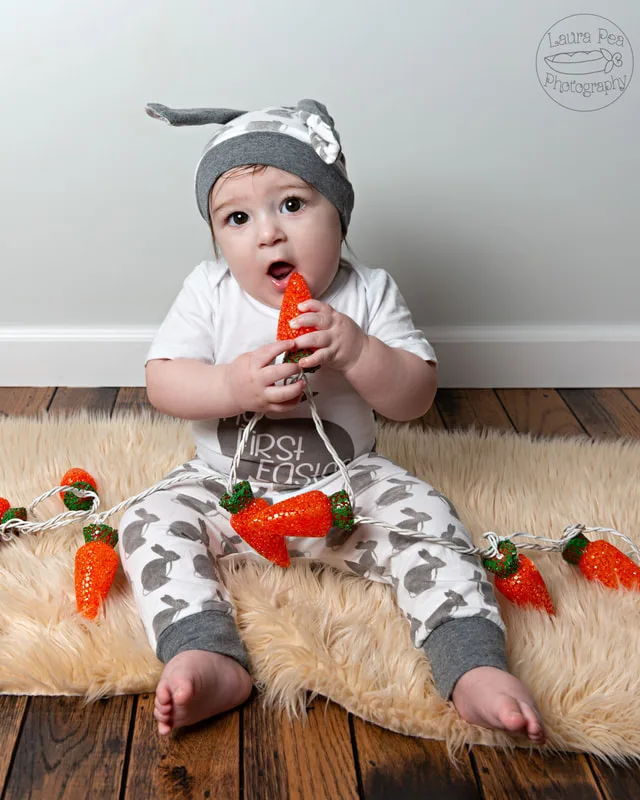 picture of baby boy's first easter photo session in an easter bunny costume putting carrot shaped lights in his mouth