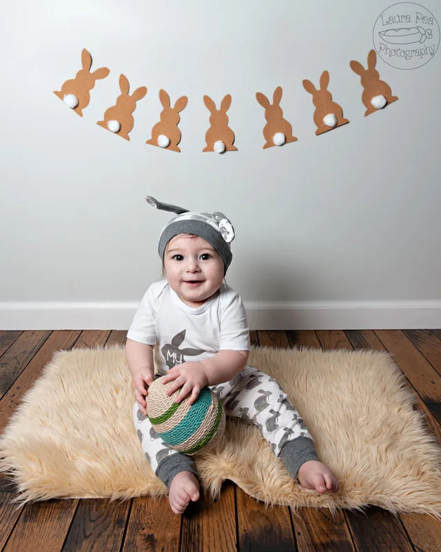 picture of baby boy's first easter photo session easter bunny costume smiling at the camera with a twine easter egg