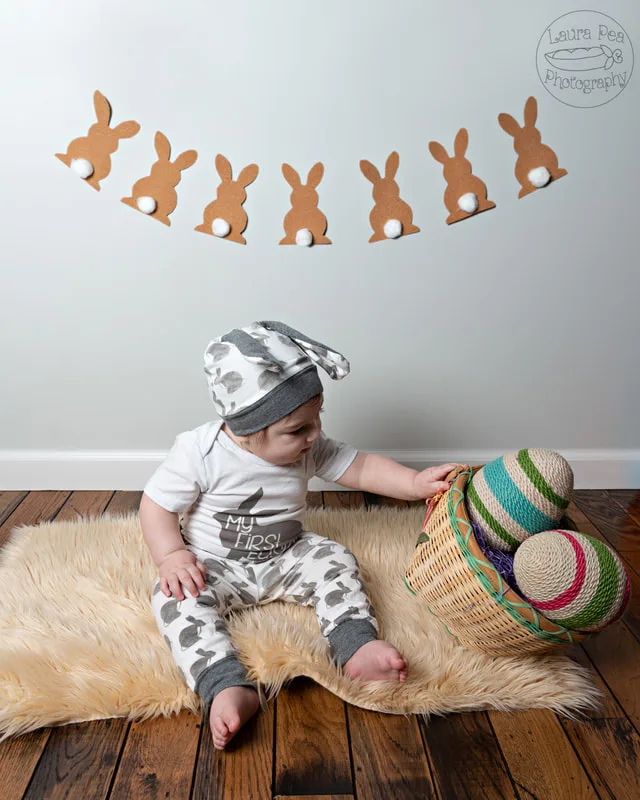  picture of baby boy's first easter photo session in an easter bunny costume knocking over twine easter eggs in a basket