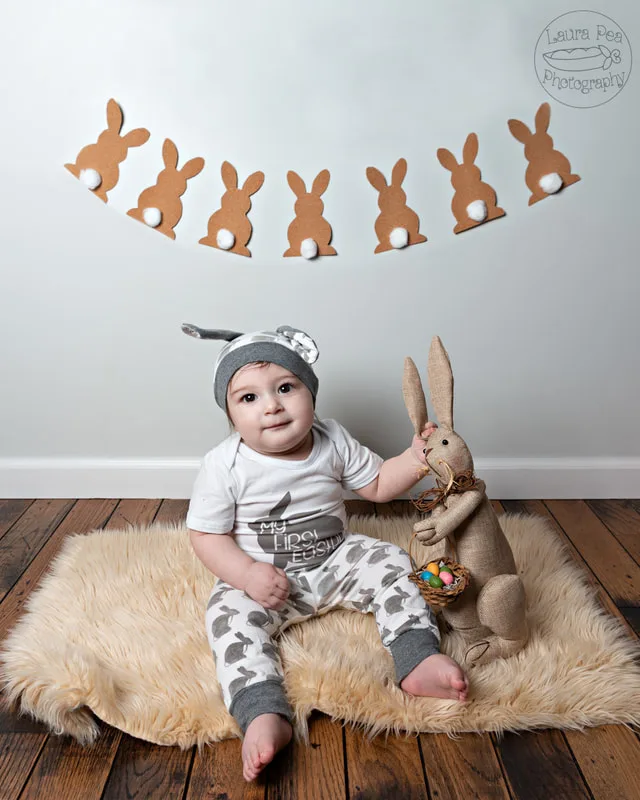 picture of baby boy's first easter photo session in an easter bunny costume smiling at the camera with a rabbit prop