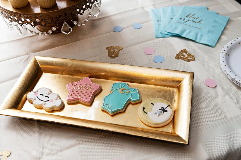 picture of colorfully decorated sugar cookies, including pink and blue onesies, clouds and a moon, on a dessert table at a gender reveal party 