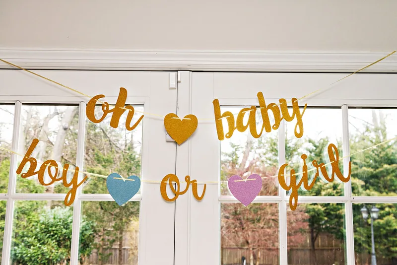 picture of a banner against a window at a gender reveal party. It reads oh baby boy or girl 