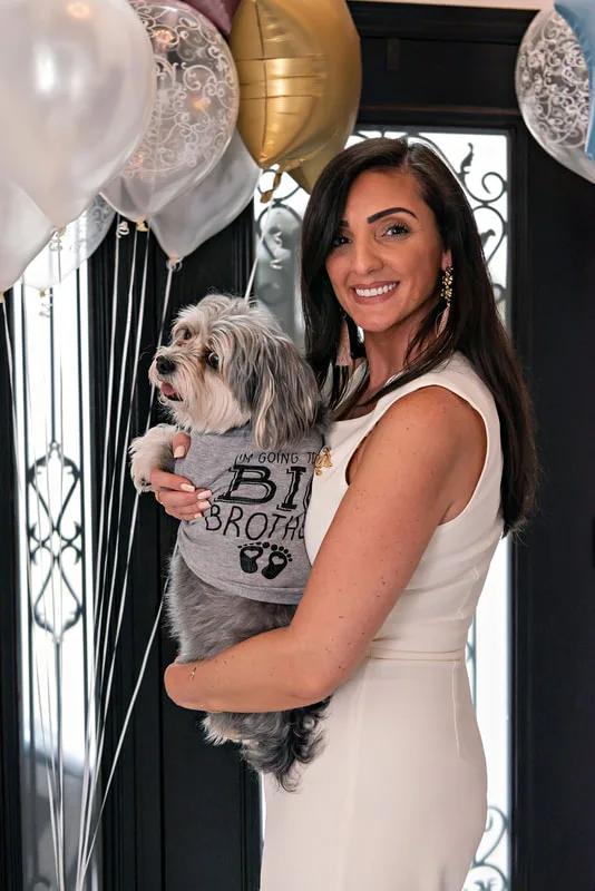 picture of a pregnant woman holding her family dog wearing a i'm going to be a big brother shirt at a gender reveal party 