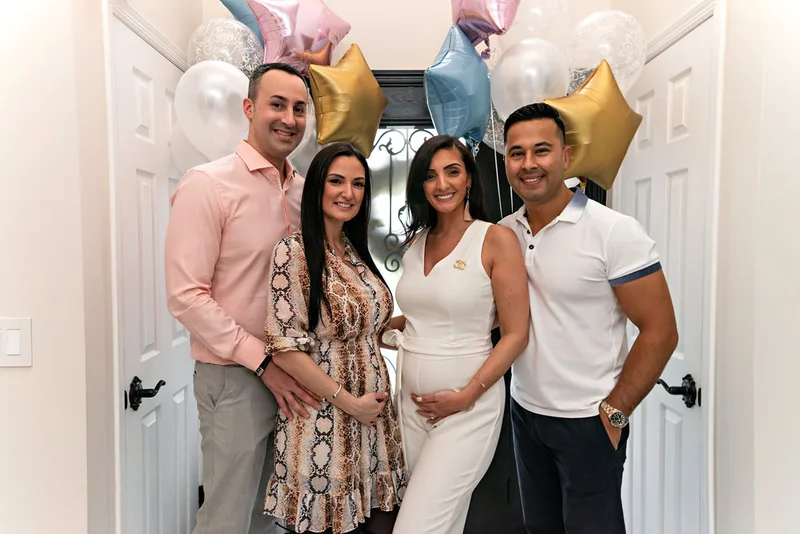 picture of two pregnant sisters with their husbands posing in a hallway at their gender reveal party