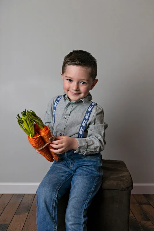 photo of a white toddler boy in an Easter outfit smiling holding carrots
