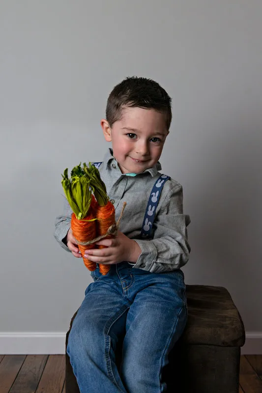 photo of a white toddler boy in an Easter outfit smiling holding carrots