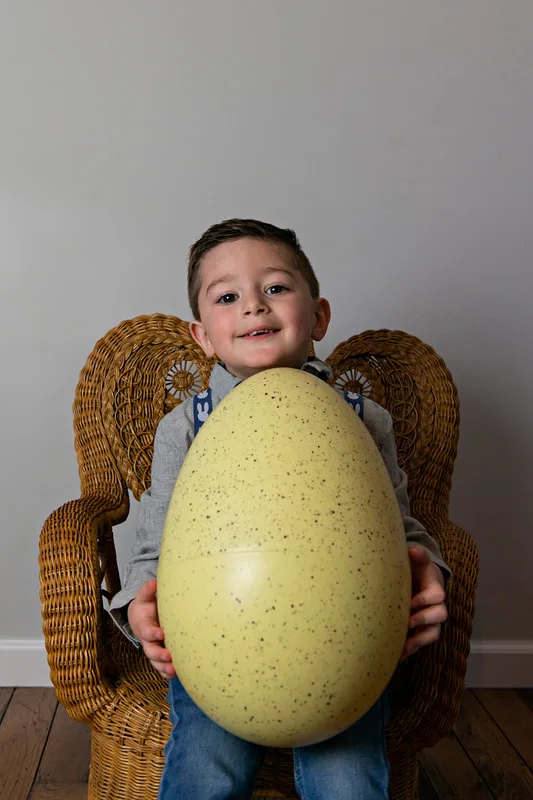 photo of a white toddler boy in an Easter outfit holding a large plastic yellow Easter egg