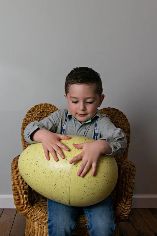 photo of a white toddler boy in an Easter outfit looking down at a large plastic Easter egg