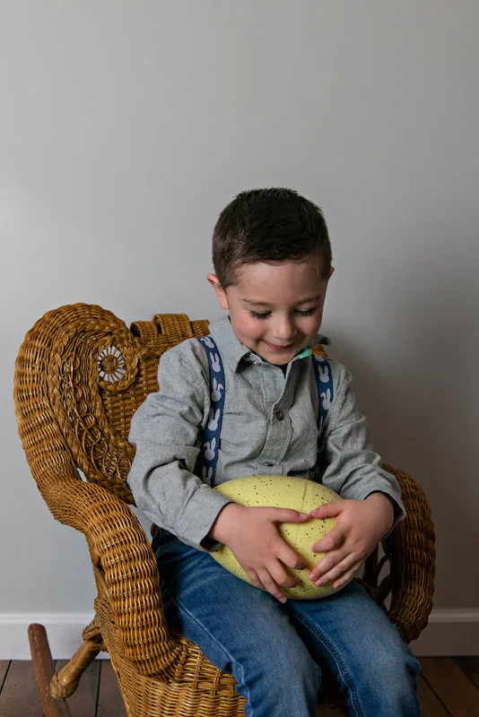 photo of a white toddler boy in an Easter outfit smiling looking down at a medium plastic Easter egg