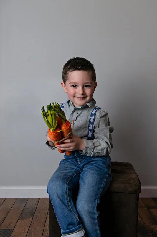 photo of a white toddler boy in an Easter outfit smiling holding carrots