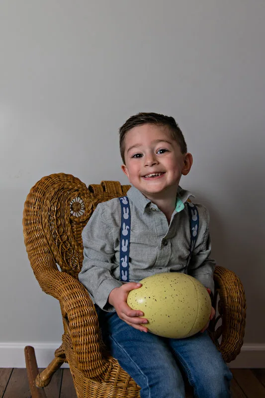 photo of a white toddler boy in an Easter outfit smiling holding a medium plastic Easter egg