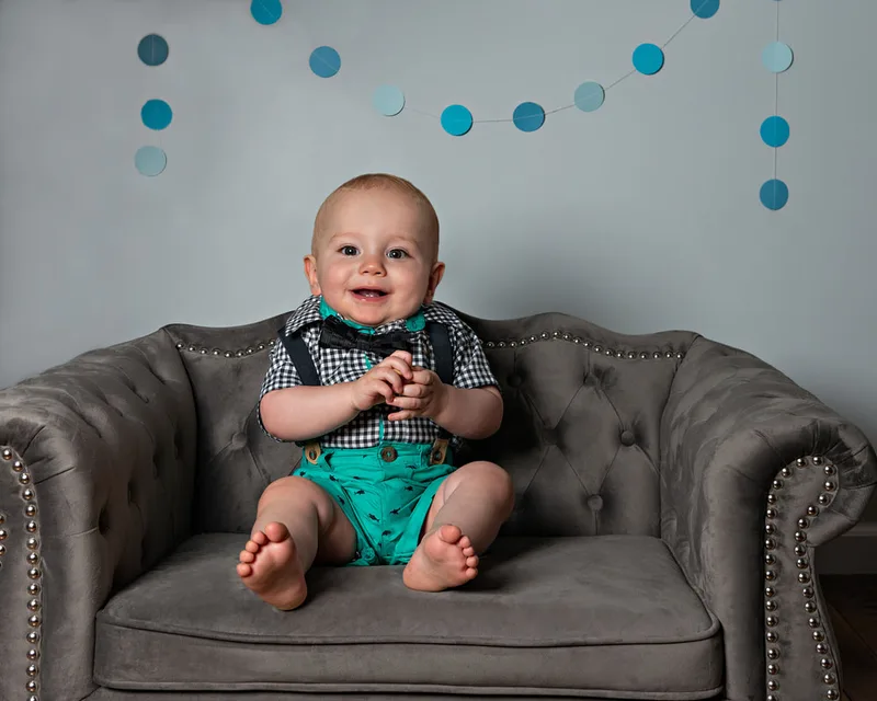 One year old boy first birthday photos on gray couch with blue dot banner