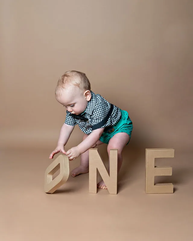 One year old twin boy with brown letters spelling one playing