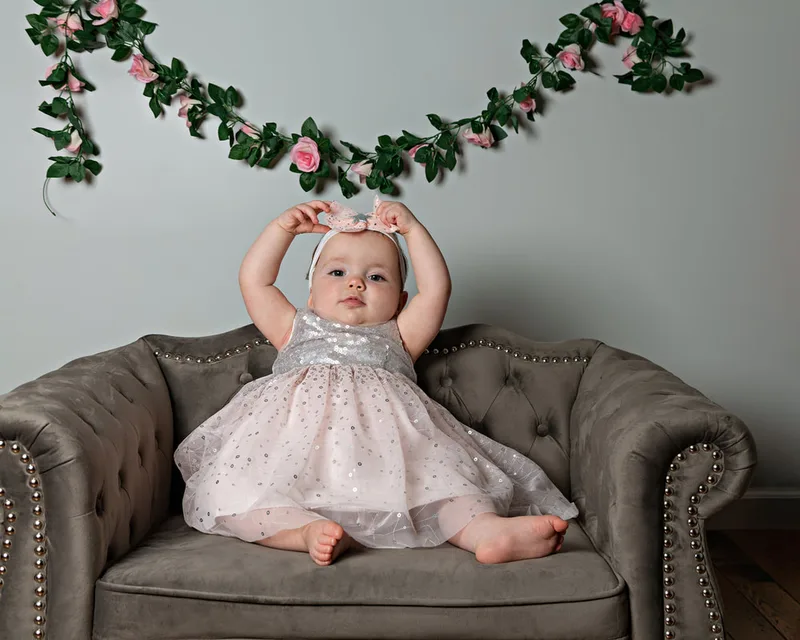 One year old twin girl first birthday photos on gray couch with pink flower garland