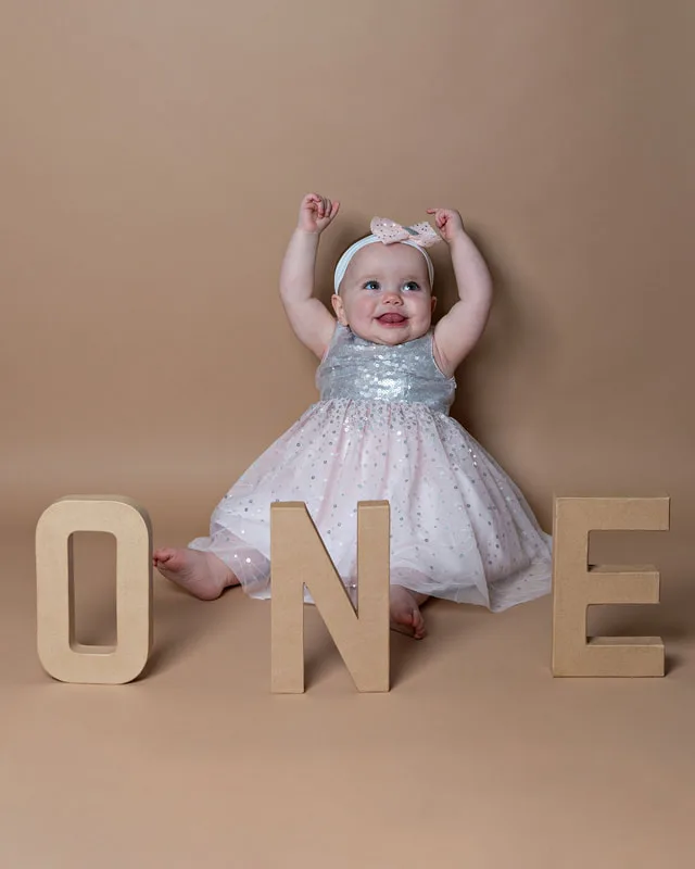 One year old twin girl smiling with brown letters spelling one