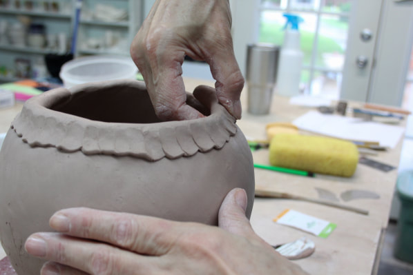 Pinching skills are handy when it comes to finalizing the top part of a coiled pottery bowl. Antoinette Badenhorst demonstrates she uses her thumb and fingers in the pinching process. She is using earthenware for the bowl.