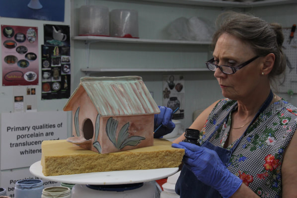Bird houses bring a variety of birds into the yard and helps to educate children on the value of nature. Antoinette Badenhorst paints a clay birdhouse that she made during the handbuilding pottery online class. The foam under the bird house is to protect the clay project but also helps to prevent the clay from dripping on the studio floor. 