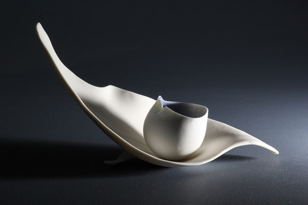Translucent porcelain pinched bowl displayed on a sculpted porcelain leaf. The natural light from the side highlights the shadows and curving of both pottery items. Made by ceramic artist Antoinette Badenhorst from Saltillo Mississippi.