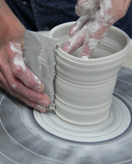 Antoinette uses a template that she made to form and shape a wheel-thrown cylinder into a porcelain mug. The picture shows her during the recording of the 