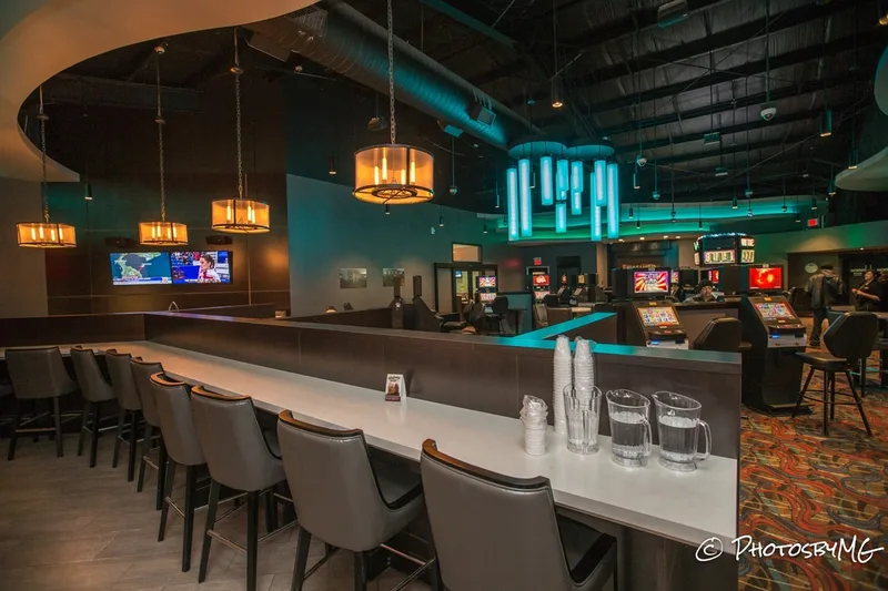 This is a shot of the gaming area from the bar. Right in front is a countertop with many chairs. Passed the little wall is the gaming area with neon lights, TVs and chairs.