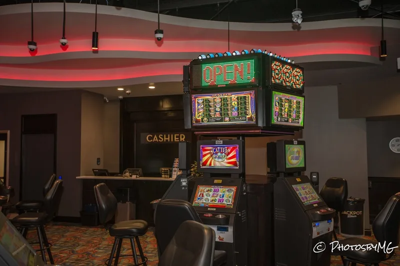 In the middle of this photo are found games set up in a square. Behind the machine is a cashier booth. The ceiling has red neon lights shining.