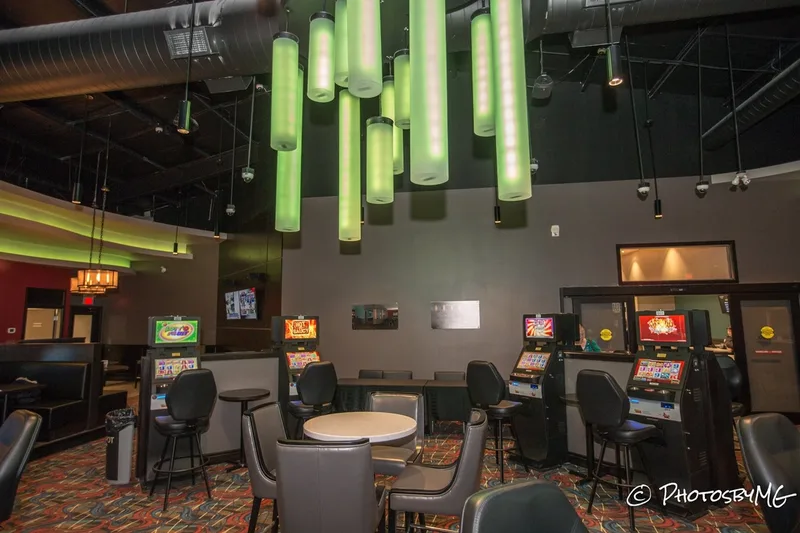 Hanging from the ceiling are skinny green neon lights. There is a table in the middle of the room and high top seated games around the room. 