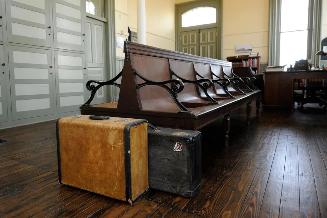 Here are some bench seats in the Military Museum . On the end of the bench are two suitcases. A tan suitcase with a black outline is in front and then there is a black suitcase behind it. 