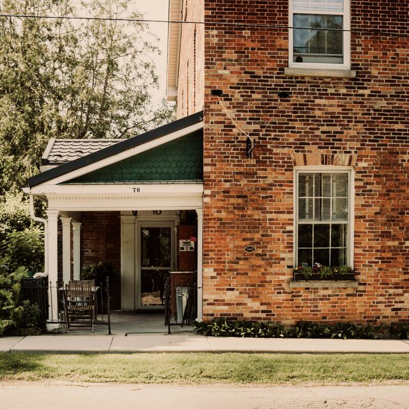 This is Cedarhurst Spa! Off centre to the left is the entrance under a right angled roof with green shingled siding. The house is covered in red, orange and black brick. 