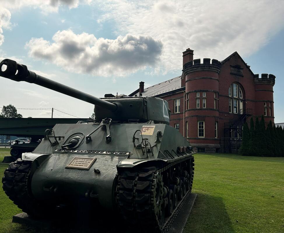 Here is a side angle of the St. Thomas Armoury.  The building is made of red brick with two rows of windows. In the front corners are large round towers. In the front of the middle is a staircase up to the second floor.
