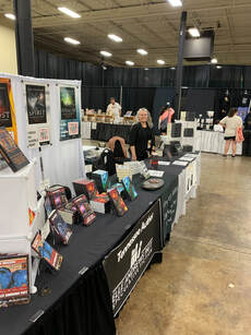 Elle at 16 foot table with mystery series and SFF anthologies