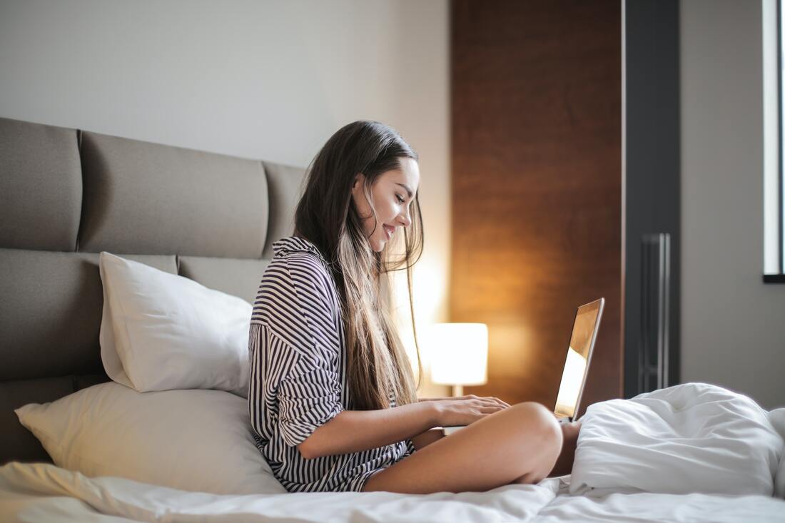 woman sitting on a bed with a laptop