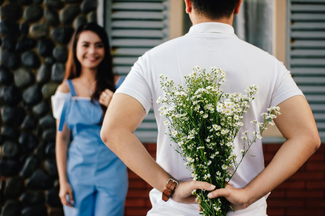 man hiding flowers from a woman
